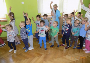 Dzieci i pracownicy przedszkola idą w kole, jeden za drugim z podniesioną ręką do góry