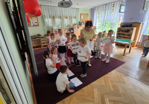 Dzieci idą z kartkami, które tworzą napis dla mamy: Jestem twoim małym przypomnieniem, że jesteś: ważna, kochana, silna, odważna, niesamowita, wyjątkowa
