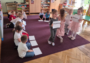 Dzieci idą z kartkami, które tworzą napis dla mamy: Jestem twoim małym przypomnieniem, że jesteś: ważna, kochana, silna, odważna, niesamowita, wyjątkowa