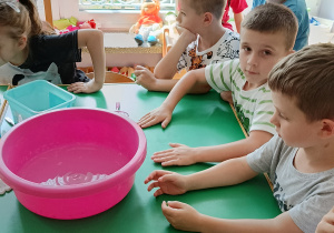 Dzieci siedzą przy stole i słuchają, jak robi się aquażelki