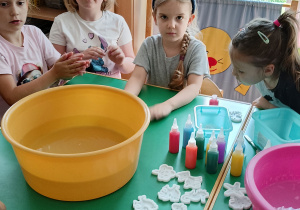 Dziewczynki siedzą przy stole i słuchają, jak robi się aquażelki