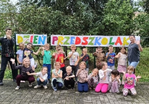 Zdjęcie grupowe dzieci z nauczycielami. W tle napis Dzień Przedszkolaka.