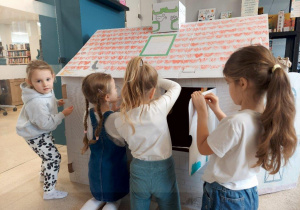 Dziewczynki malują kredkami kartonowy domek