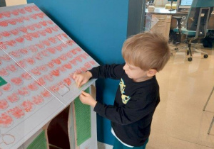 Chłopiec maluje kredkami kartonowy domek