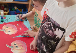 Dzieci wykonują pracę plastyczną - ozdabiają papierowe dynie.