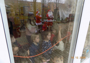 Dzieci oglądają oglądają przez szyby okienne prezenty od Mikołaja