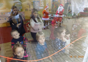Dzieci oglądają oglądają przez szyby okienne prezenty od Mikołaja