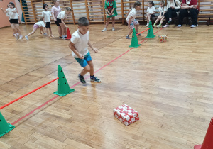 Dzieci biorą udzaił w konkurencji sportowej z paczką prezentów.