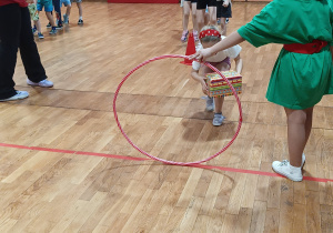 Dziewczynka przechodzi przez koło hula-hop z paczką prezentową.