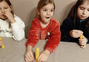 Dzieci siedzą przy stole i prezentują swoje wykonane własnoręcznie świece.