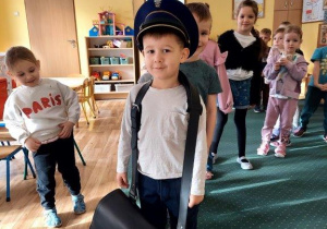 Chłopiec z torbą listonosza oraz ubrany w czapkę listonosza.