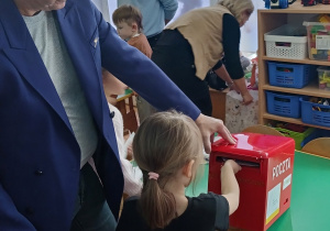 Dziewczynka wrzuca list do skrzynki pocztowej.