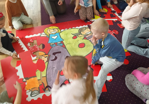 Dzieci układają gigantyczne puzzle w kształcie znaczka pocztowego.