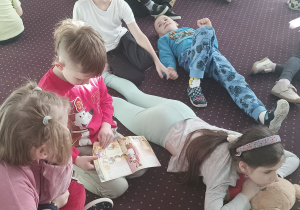 Dzieci leżą na dywanie i słuchają bajki