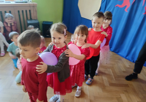 Pięcioro dzieci stoi jeden za drugim. Mają między sobą balon. Szykują się do wyścigu z balonami.