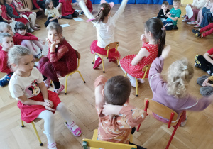 Sześcioro dzieci siedzi na krzesłach. Przygotowują się do konkurencji podawania balonika