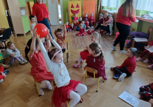 Sześcioro dzieci siedzi na krzesłach w kole. Podają sobie balon.