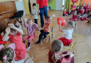 Sześcioro dzieci siedzi na krzesłach w kole. Podają sobie balon.