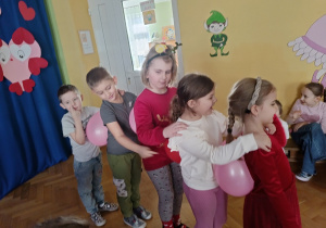 Pięcioro dzieci stoi jeden za drugim. Mają między sobą balon. Szykują się do wyścigu z balonami.
