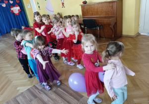 Dzieci w dwóch drużynach po pięcioro, ustawione jeden za drugi ścigają się z balonami ściśniętymi między sobą.