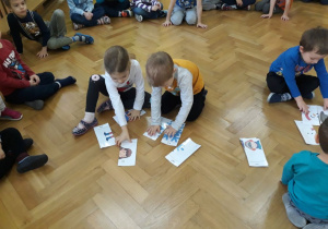 Dzieci siedzą w kole. Wybrane dzieci w parach układają obrazek z pociętych części