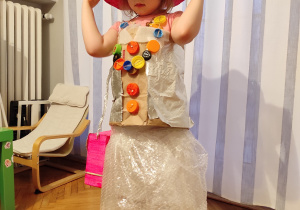 Dziewczynka w kapeuszu wykonanym z bibuły i w sukience z papieru pakownego, folii bąbelkowej oraz plastikowych korków