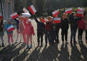 Dzieci z grupy trzeciej stoją na tarasie z flagami w rękach