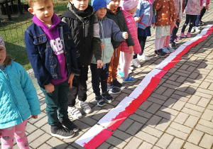 Dzieci z grupy czwartej stoją przed flagami