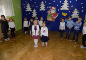 Dwie dziewczynki stoją na środku sali i mówią świąteczny wiersz. Pozostałe dzieci stoją za nimi w półkolu.