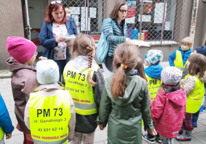 Dzieci stoją przed budynkiem poczty. Nauczycielki rozdają przygotowane wcześniej listy.