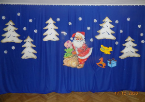 Mikołaj i białe choinki na niebieskim materiale jako dekoracja do występu.