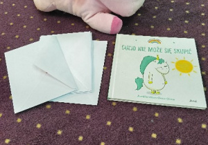 Zdjęcie maskotki jednorożca, książki oraz koperty z zadaniami